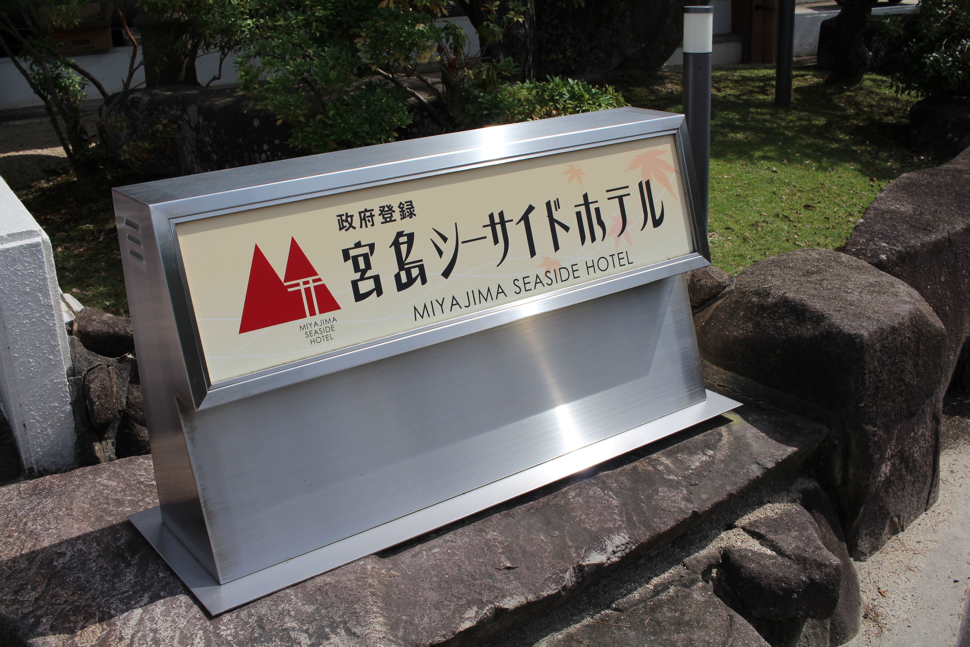 Un cartel del Hotel Miyajima Seaside con un logotipo rojo y texto en japonés.