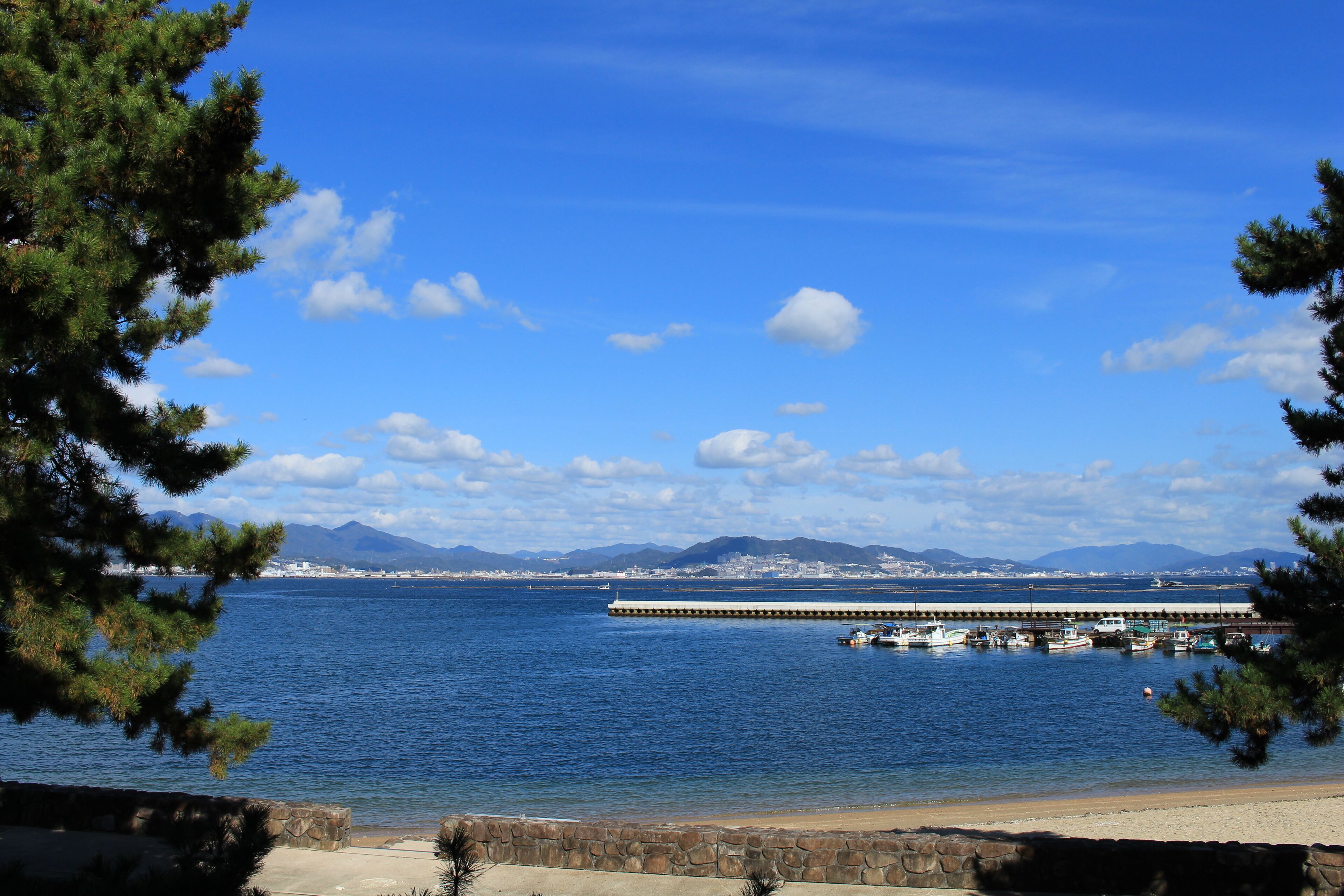 A coastal view with a pier extending into the water, surrounded by mountains and a clear sky.