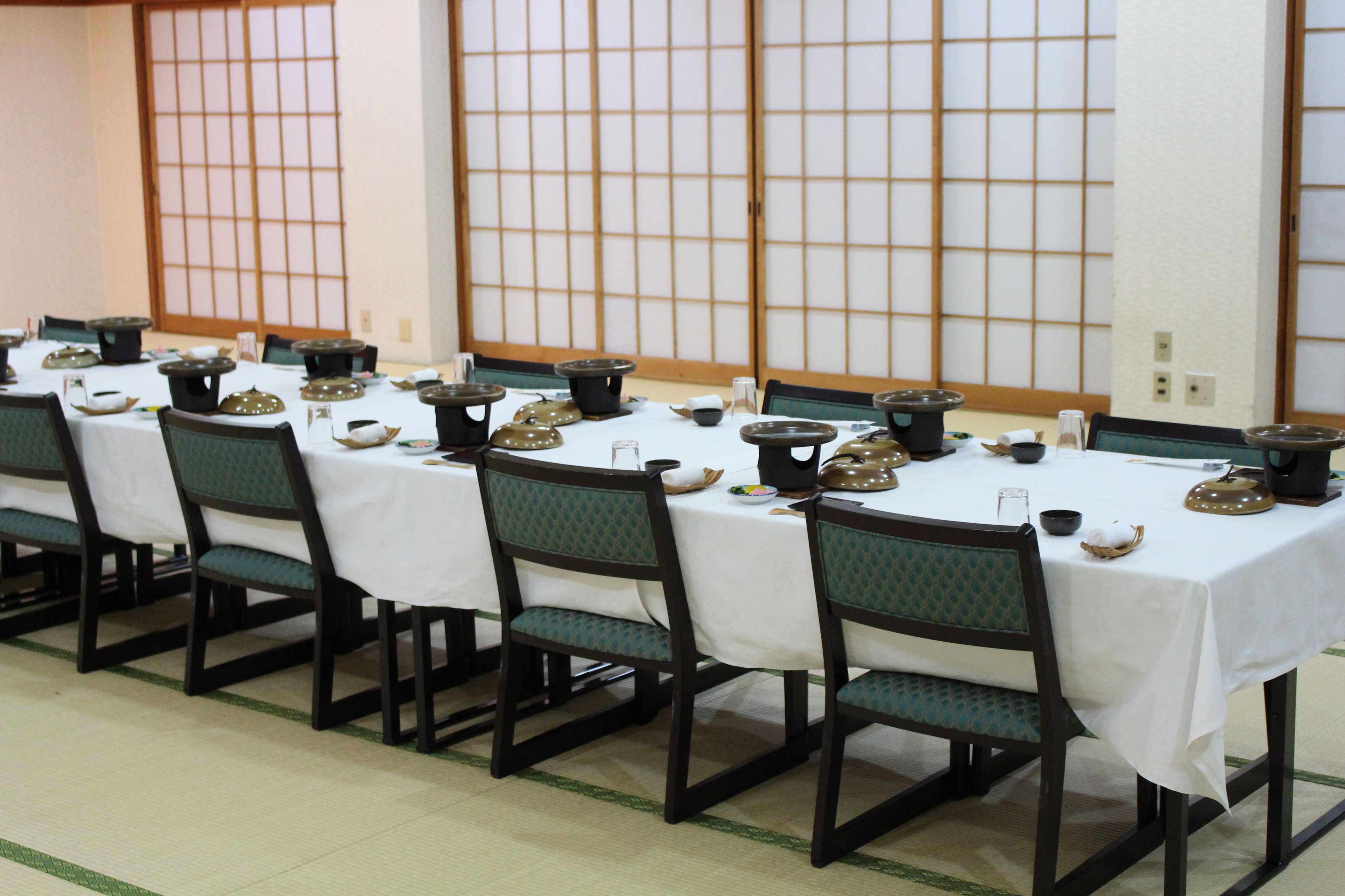 A traditional Japanese dining room with tatami mats, low tables, and green cushioned chairs.