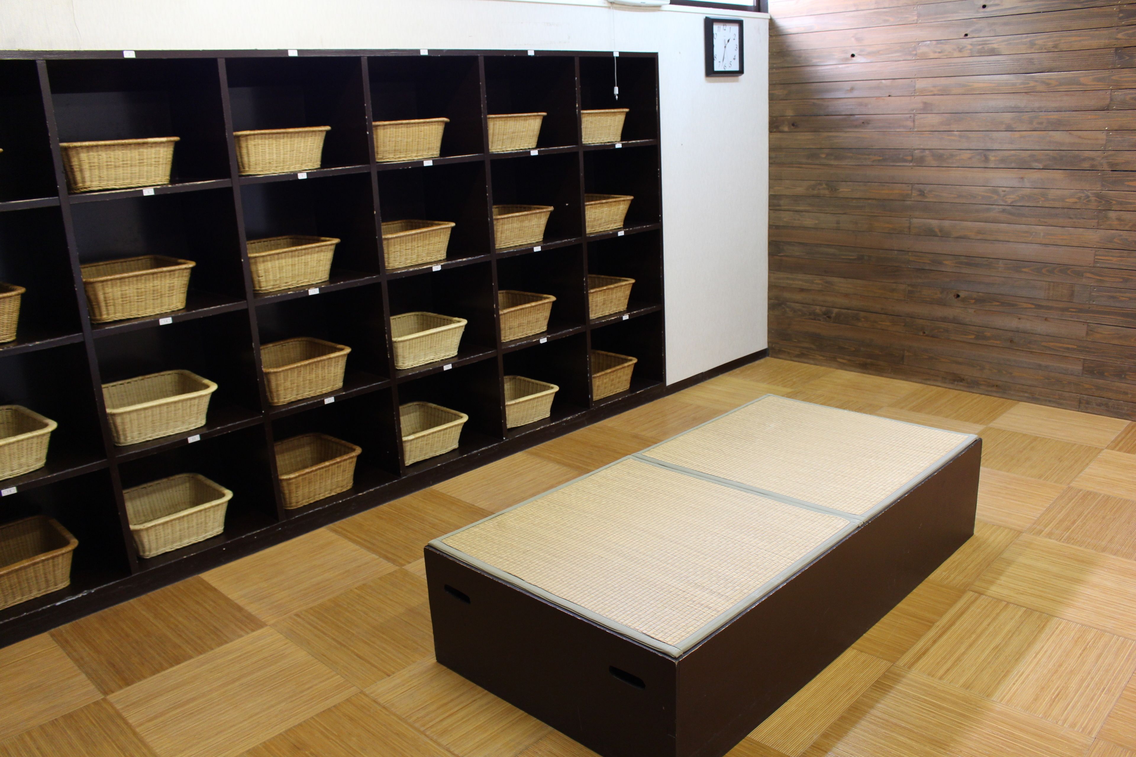 Una habitación con piso de madera, repisas con cestas y un futón de tatami.
