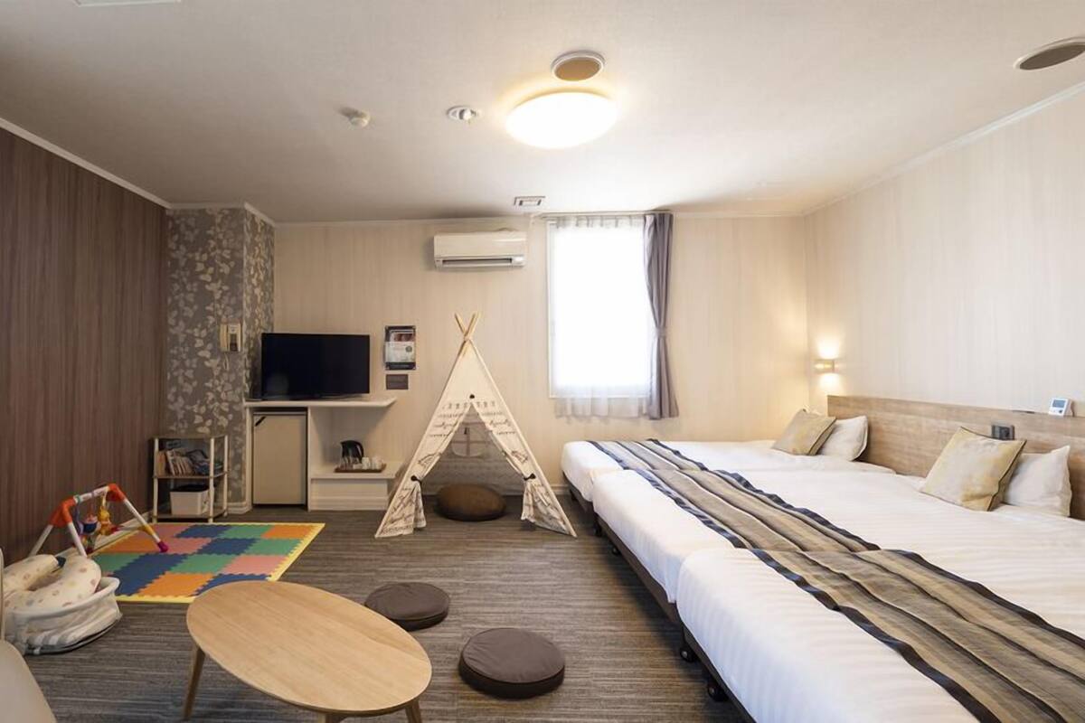 Una habitación de hotel con cama, televisión, escritorio, silla, mesita, tienda de campaña y ventana.