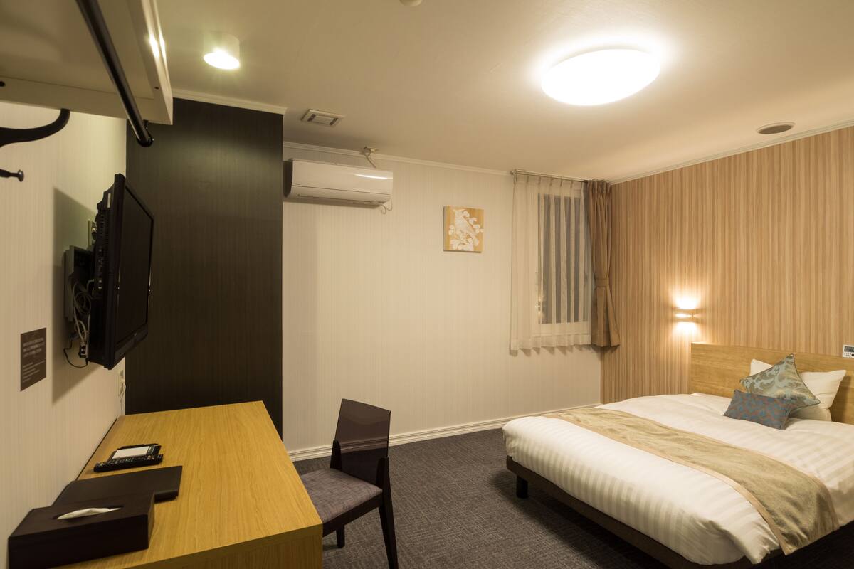 Una habitación de hotel con cama, escritorio, silla, televisor y aire acondicionado.