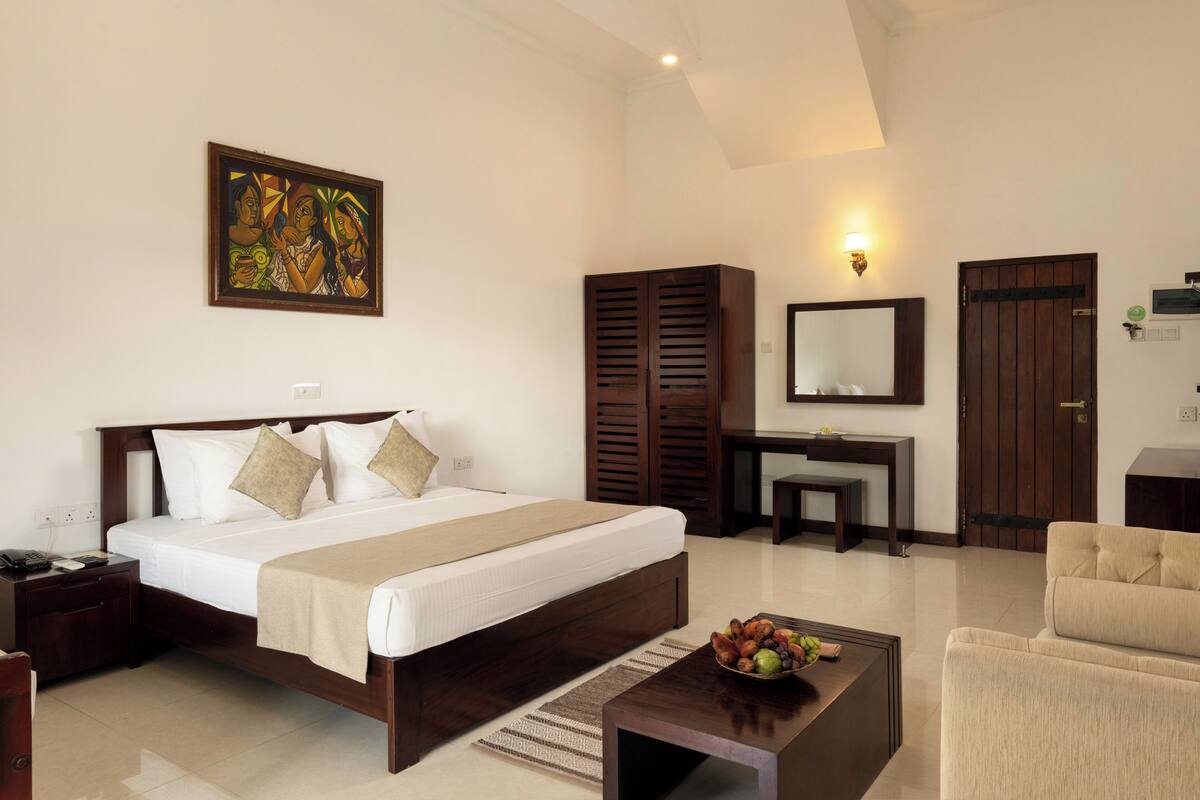 A hotel room with a bed, a desk, a chair, a coffee table, and a painting on the wall.