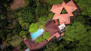 Vue aérienne d’une propriété comprenant plusieurs bâtiments aux toits rouges, une piscine et une végétation luxuriante.