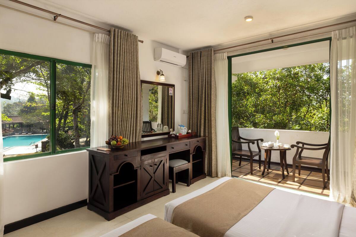 A hotel room with a bed, desk, chair, and a balcony with a pool view.