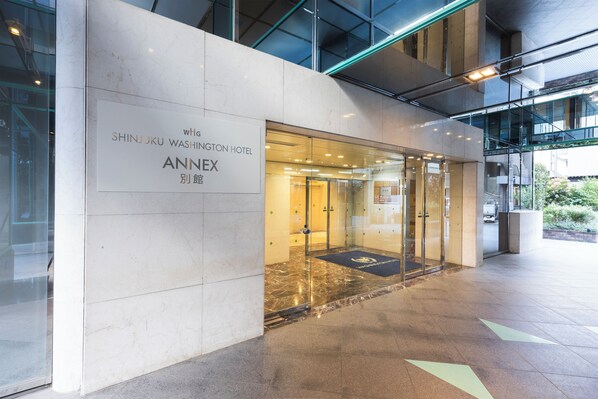 The entrance to the Shinjuku Washington Hotel Annex with a marble facade, glass doors, and a black doormat with the hotel logo. - Shinjuku Washington Hotel Annex (Tokyo)