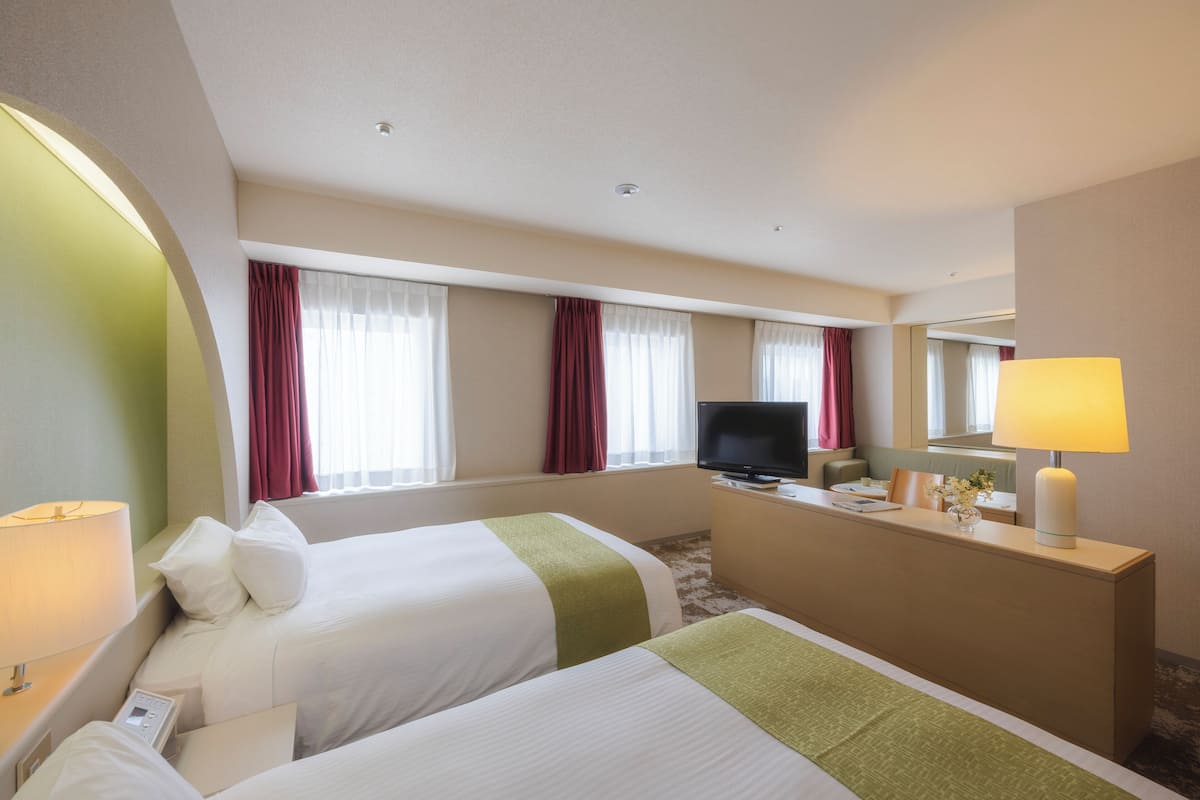 Ein Hotelzimmer mit zwei Betten, einem Schreibtisch, einem Fernseher und einer Lampe.