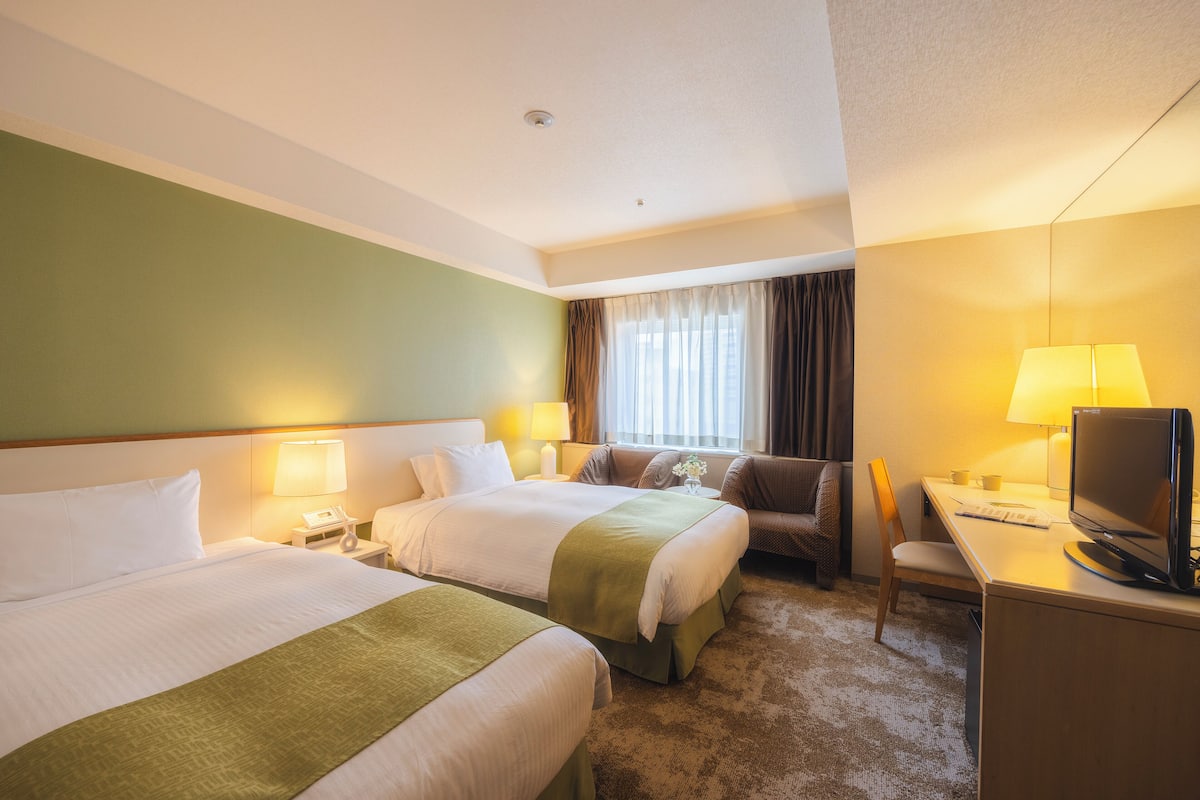 Ein Hotelzimmer mit zwei Betten, einem Schreibtisch mit Computer, einem Stuhl und einem Fernseher.