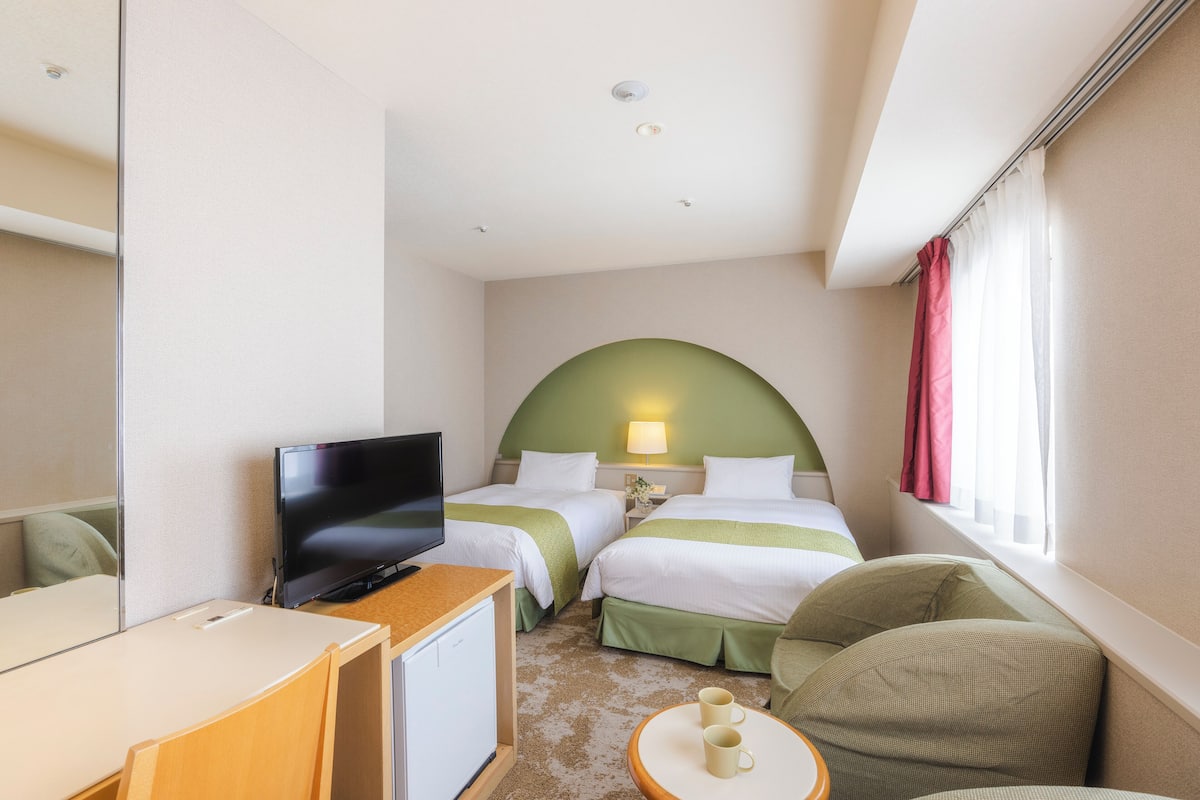 Ein Hotelzimmer mit zwei Betten, einem Fernseher, einem Schreibtisch und einem kleinen Tisch mit Tassen.