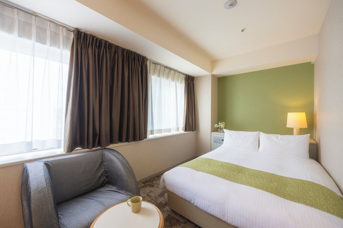Ein Hotelzimmer mit Bett, Sessel, Tisch mit Tasse und Lampe.