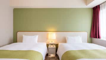 A hotel room with two beds, a nightstand with a lamp, and a window with curtains.