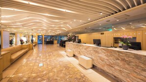Un rebedor d'hotel modern amb un taulell de recepció de marbre, zona de seients i un disseny de sostre corbat.