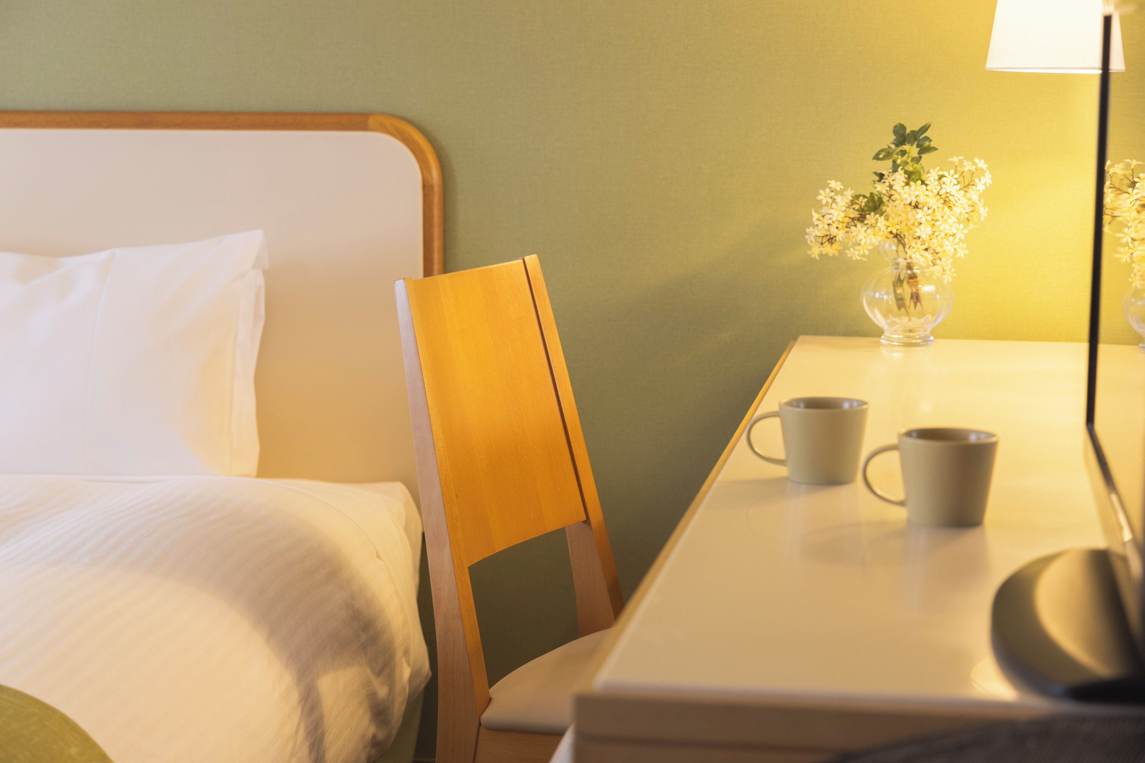 Ein Hotelzimmer mit einem Bett, einem Holzstuhl, einem Tisch mit zwei Tassen und einer Vase mit Blumen.