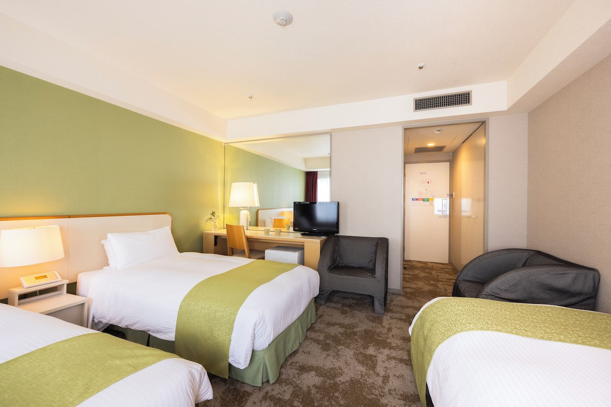Ein Hotelzimmer mit zwei Betten, einem Schreibtisch, einem Fernseher und einem Sessel.