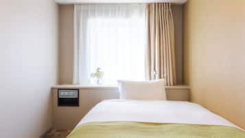 A hotel room with a bed, a window with curtains, a bedside table with a vase of flowers, and a wall-mounted control panel.