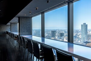 A modern conference room with a long table and chairs, large windows offering a city view.