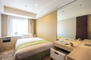 A hotel room with a bed, a desk, a mirror, and a window with curtains.