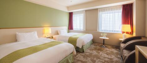 A hotel room with two beds, a small table, a chair, and a window with curtains.