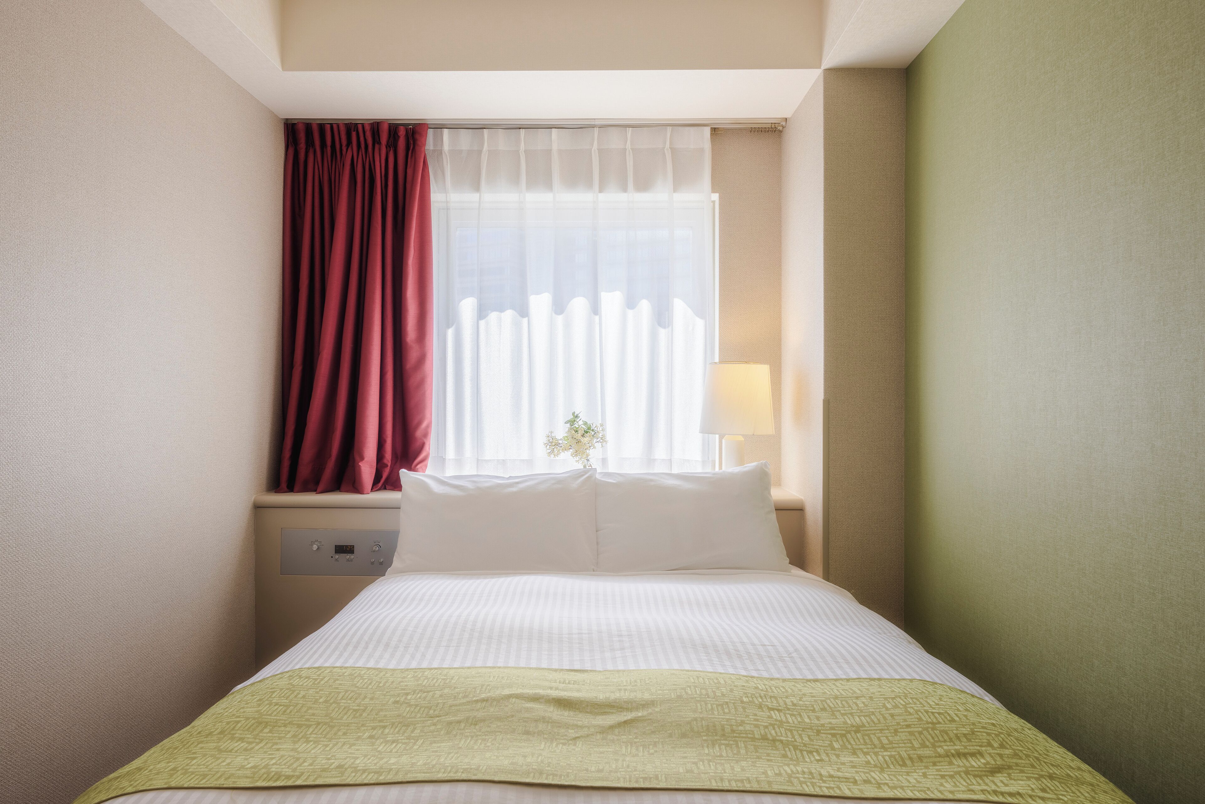 A hotel room with a bed, a nightstand, a lamp, and a window with curtains.