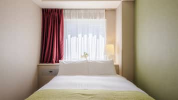 A hotel room with a bed, a nightstand, a lamp, and a window with curtains.