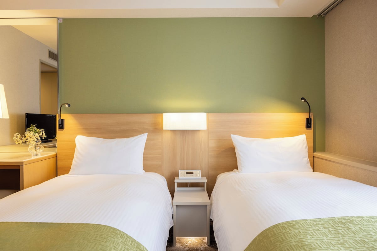 Ein Hotelzimmer mit zwei Betten, einem Nachttisch mit Lampe und einer digitalen Uhr.