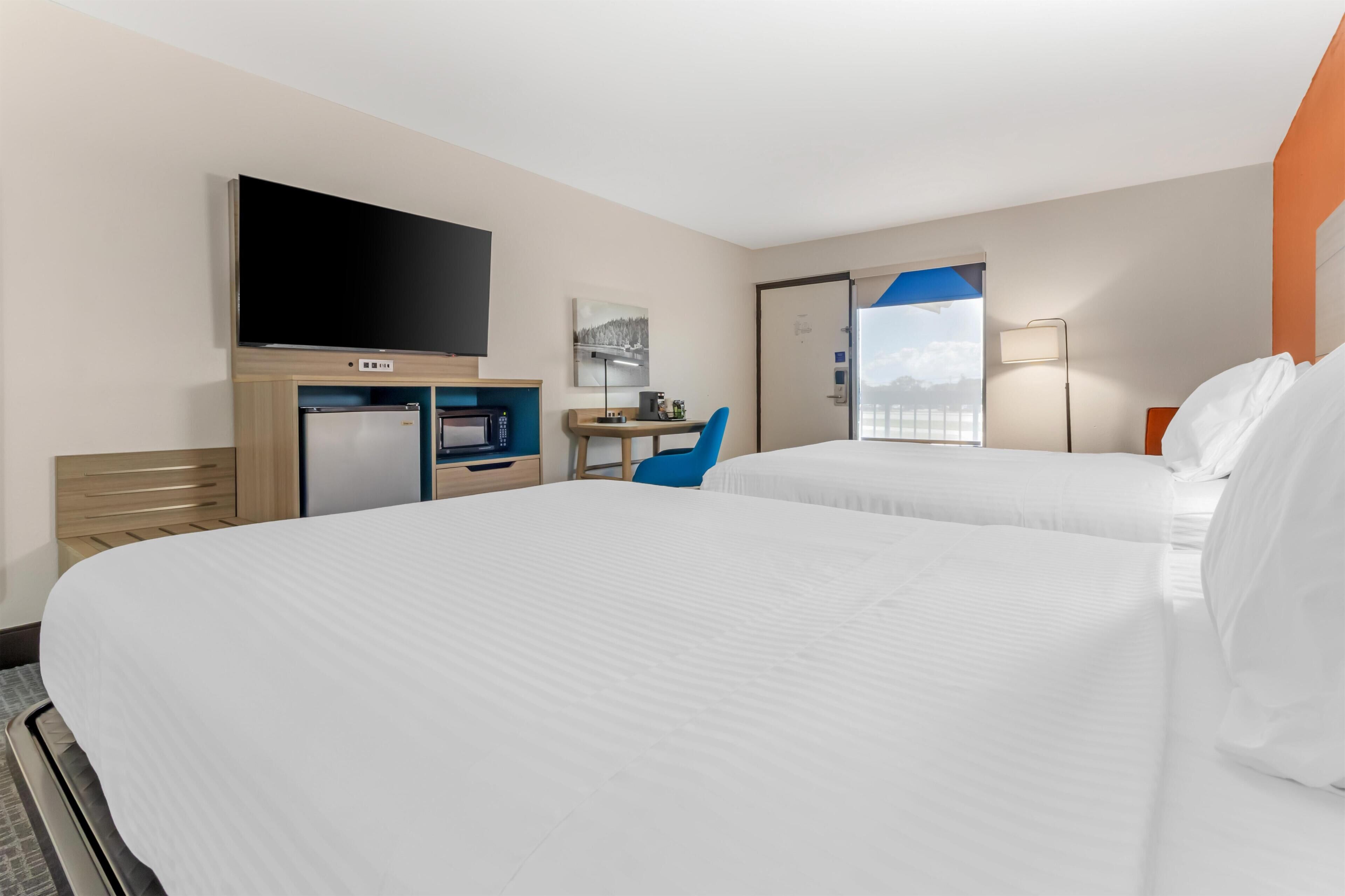 Habitación de hotel con dos camas, un escritorio, una televisión y una ventana con vistas.