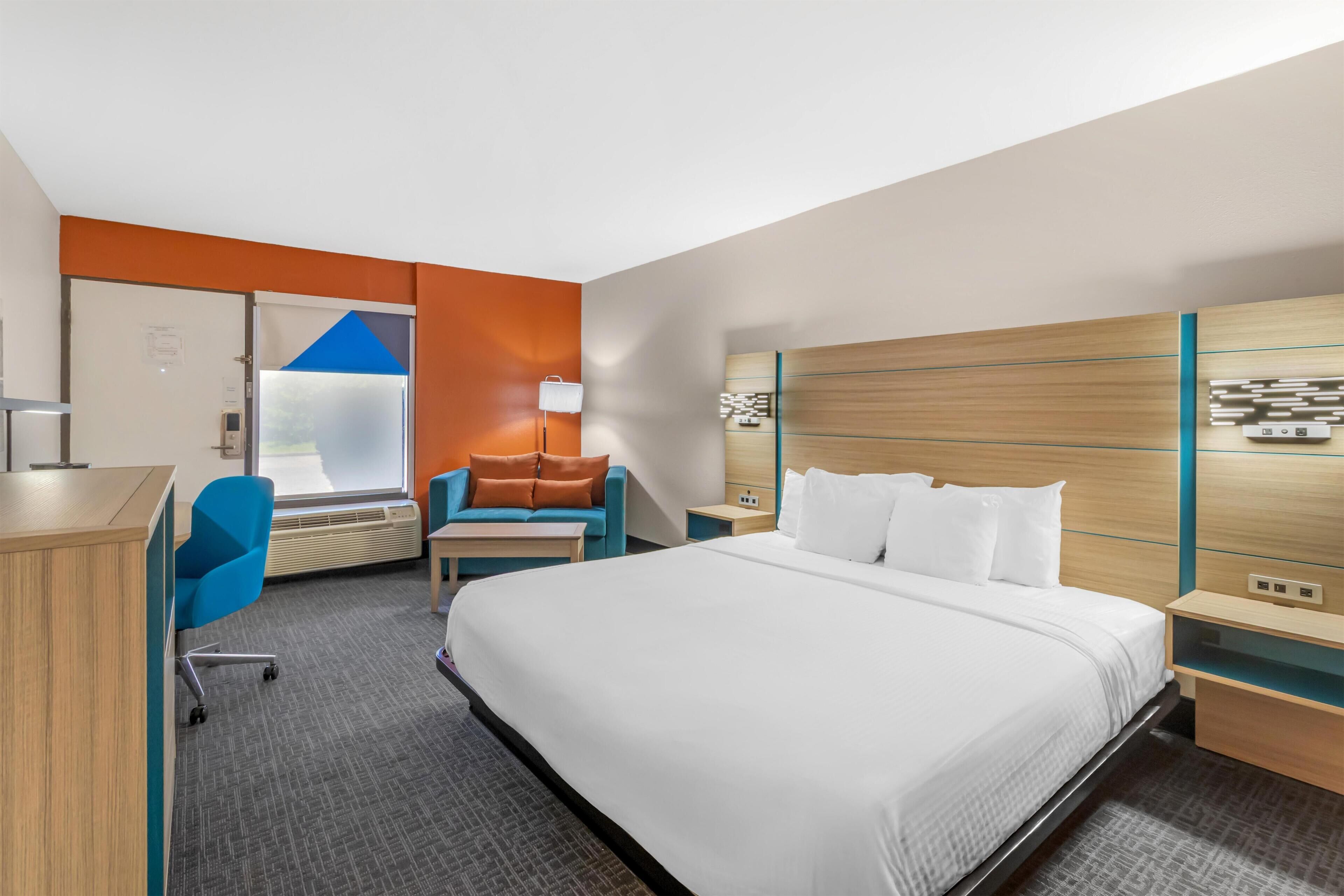 A hotel room with a bed, a desk, a chair, a sofa, a nightstand, and a wall-mounted TV.