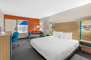 Habitación de hotel con cama, escritorio, silla, sofá, mesita de noche y televisión montada en la pared.