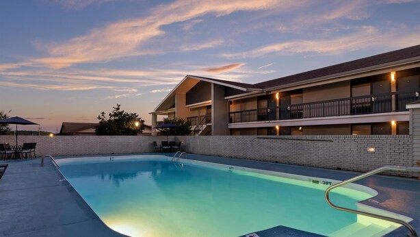 A swimming pool with a 3-foot depth marker, a covered patio area with outdoor seating, and a building with multiple balconies.