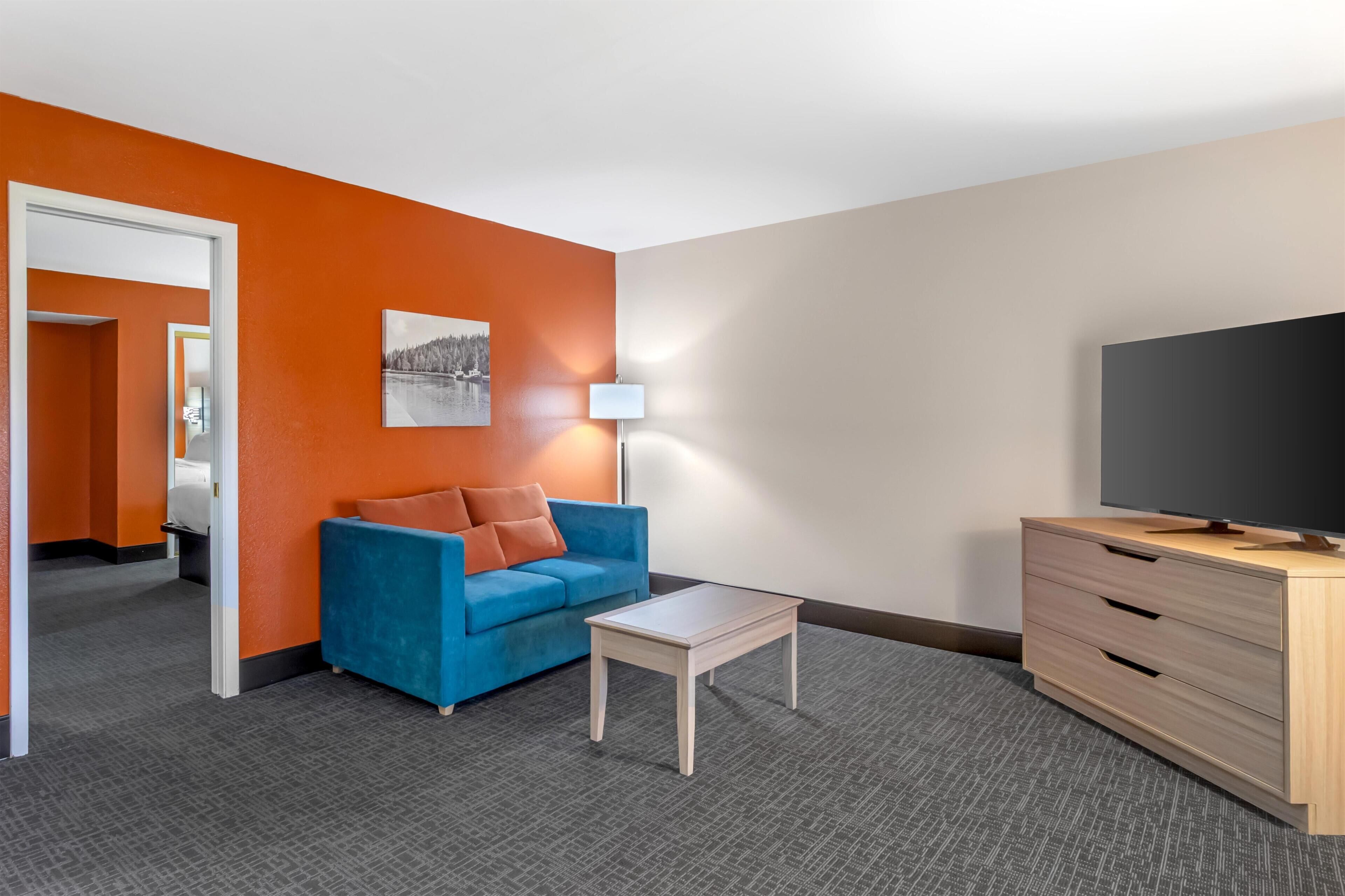 A hotel room with a blue sofa, a small white table, a TV, and a wooden cabinet.