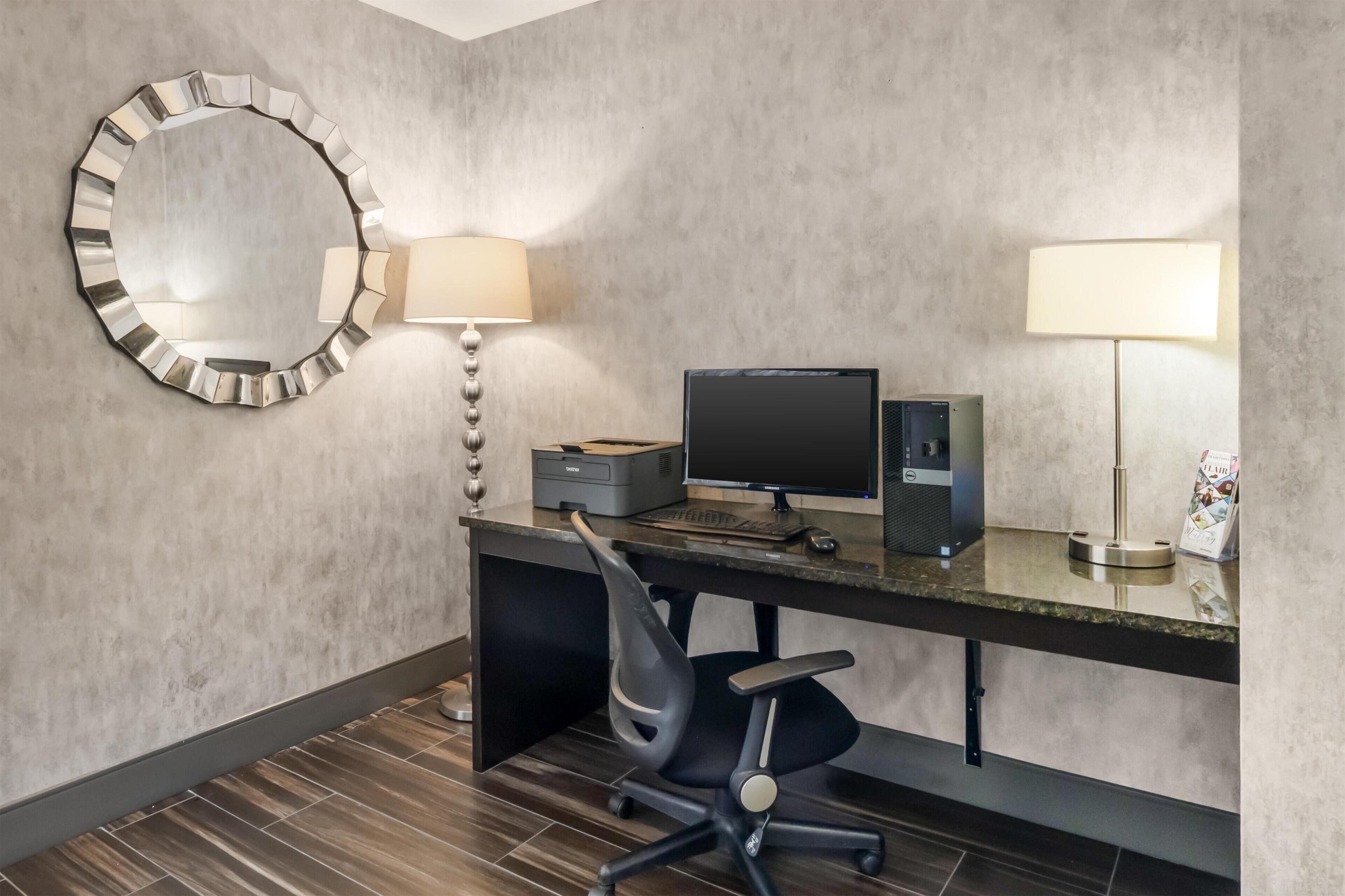 A hotel room with a desk, computer, chair, and two lamps.