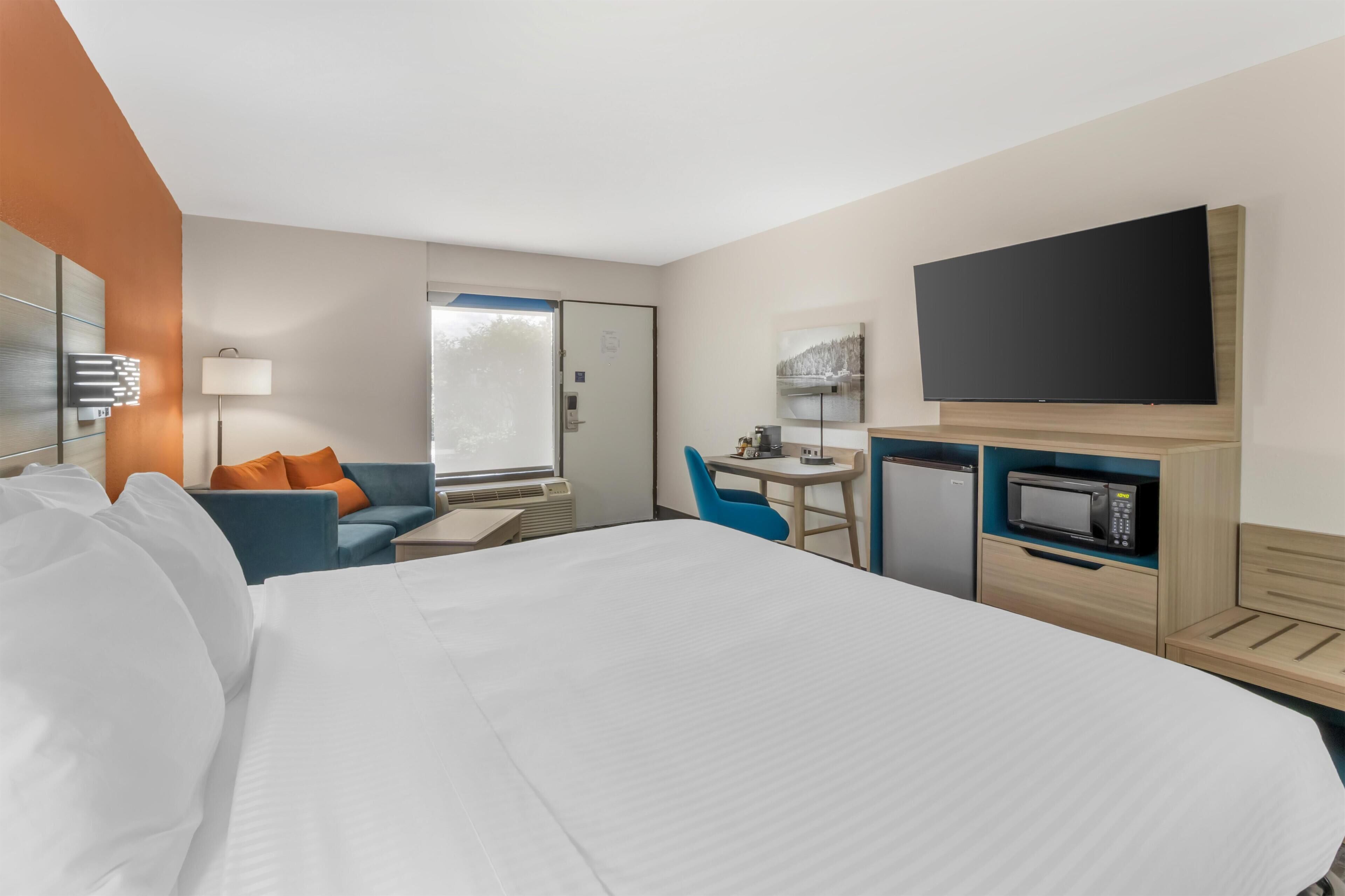 A hotel room with a bed, a desk, a chair, a television, and a microwave.