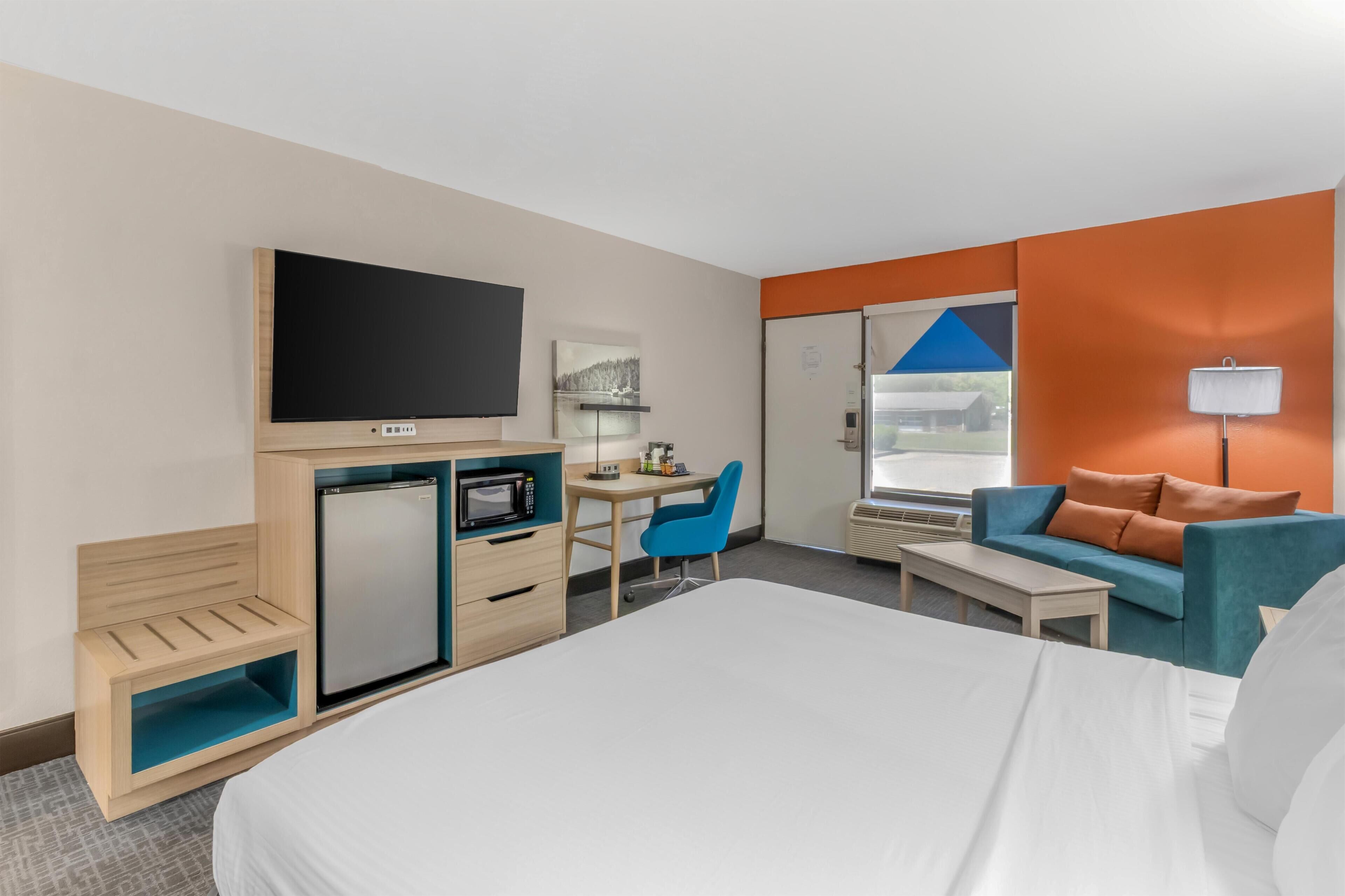 A hotel room with a bed, a desk with a chair, a television, a microwave, and a small refrigerator.