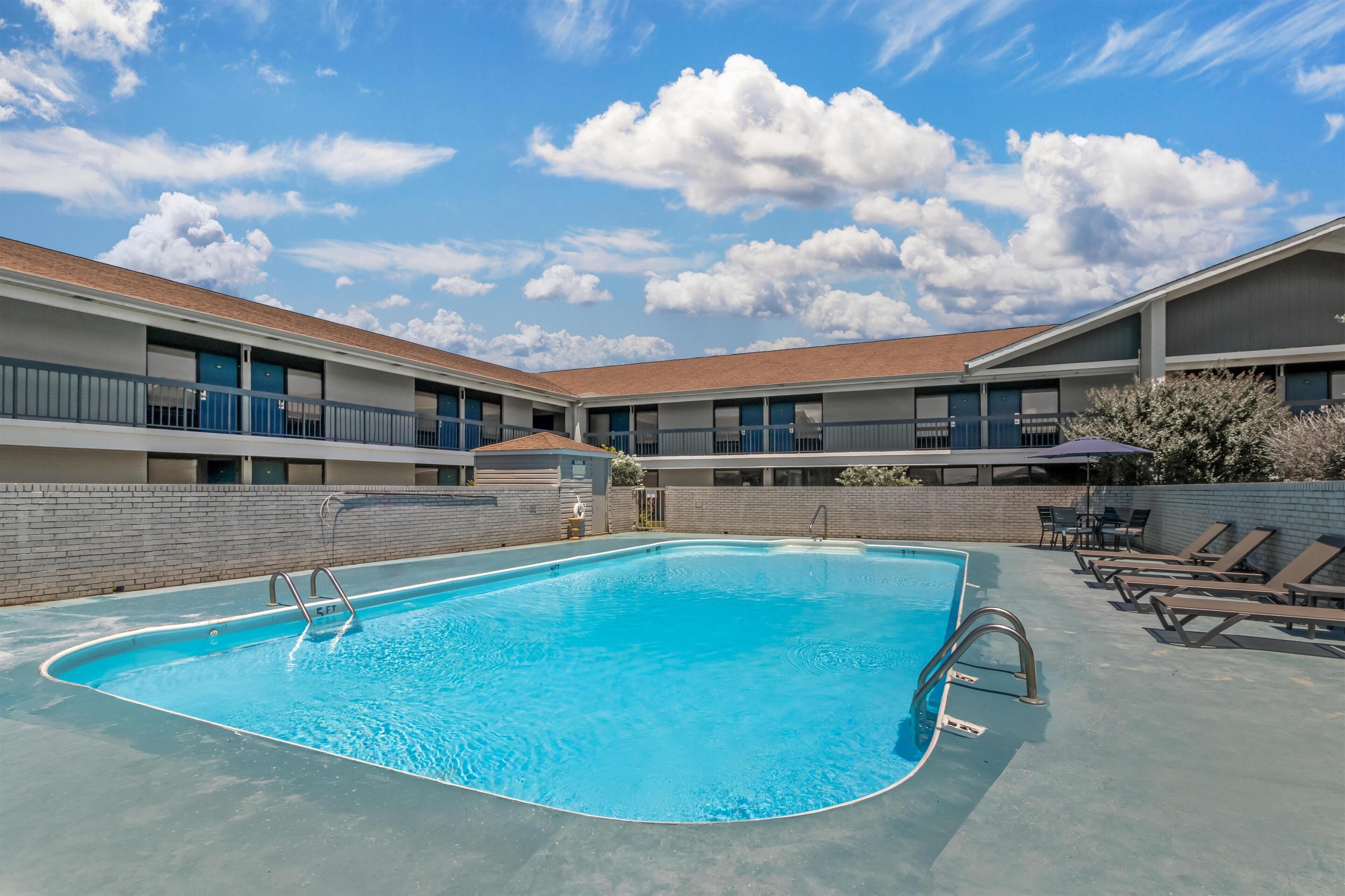 A swimming pool with a blue water feature, surrounded by a brick wall, and adjacent to a building with multiple windows and balconies.