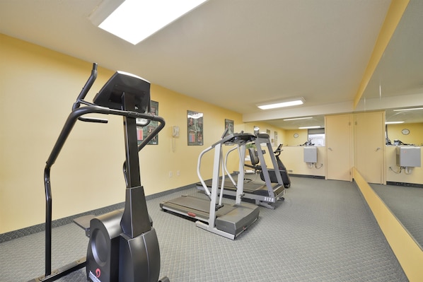 Une salle de sport équipée de tapis de course et d’appareils elliptiques, avec un miroir et des casiers.