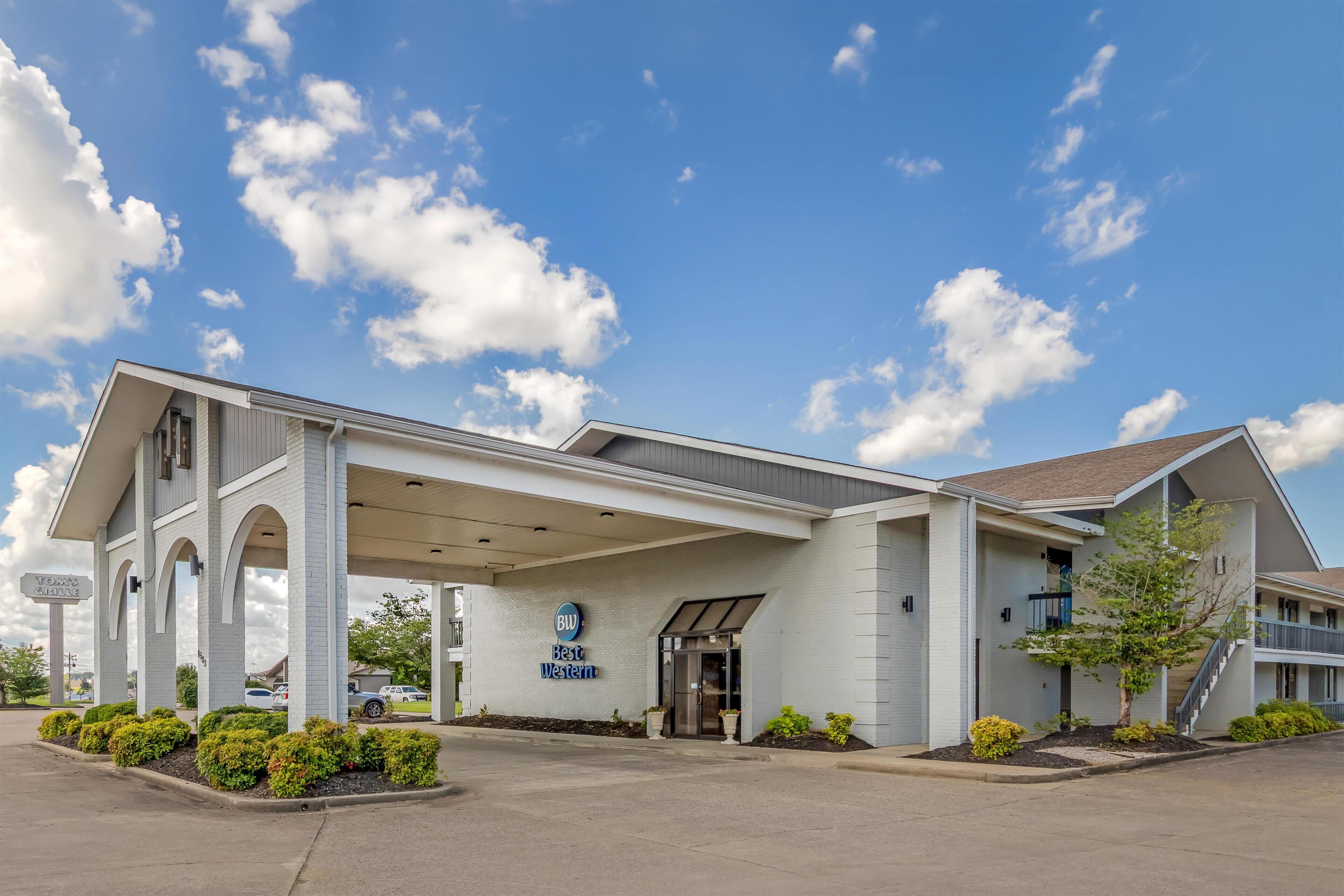 Un hotel con entrada cubierta, un letrero de 'Best Western' y un estacionamiento.