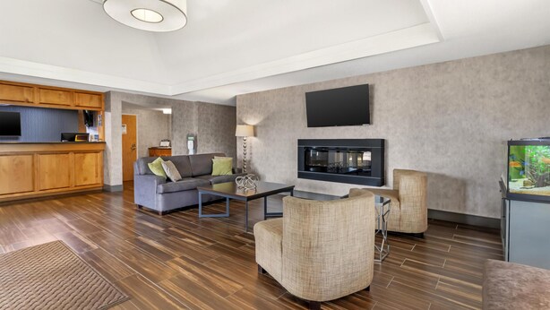 A modern living room with a sofa, armchairs, a coffee table, a flat-screen TV, and a kitchen area with wooden cabinets. - Best Western University Inn (Murray)