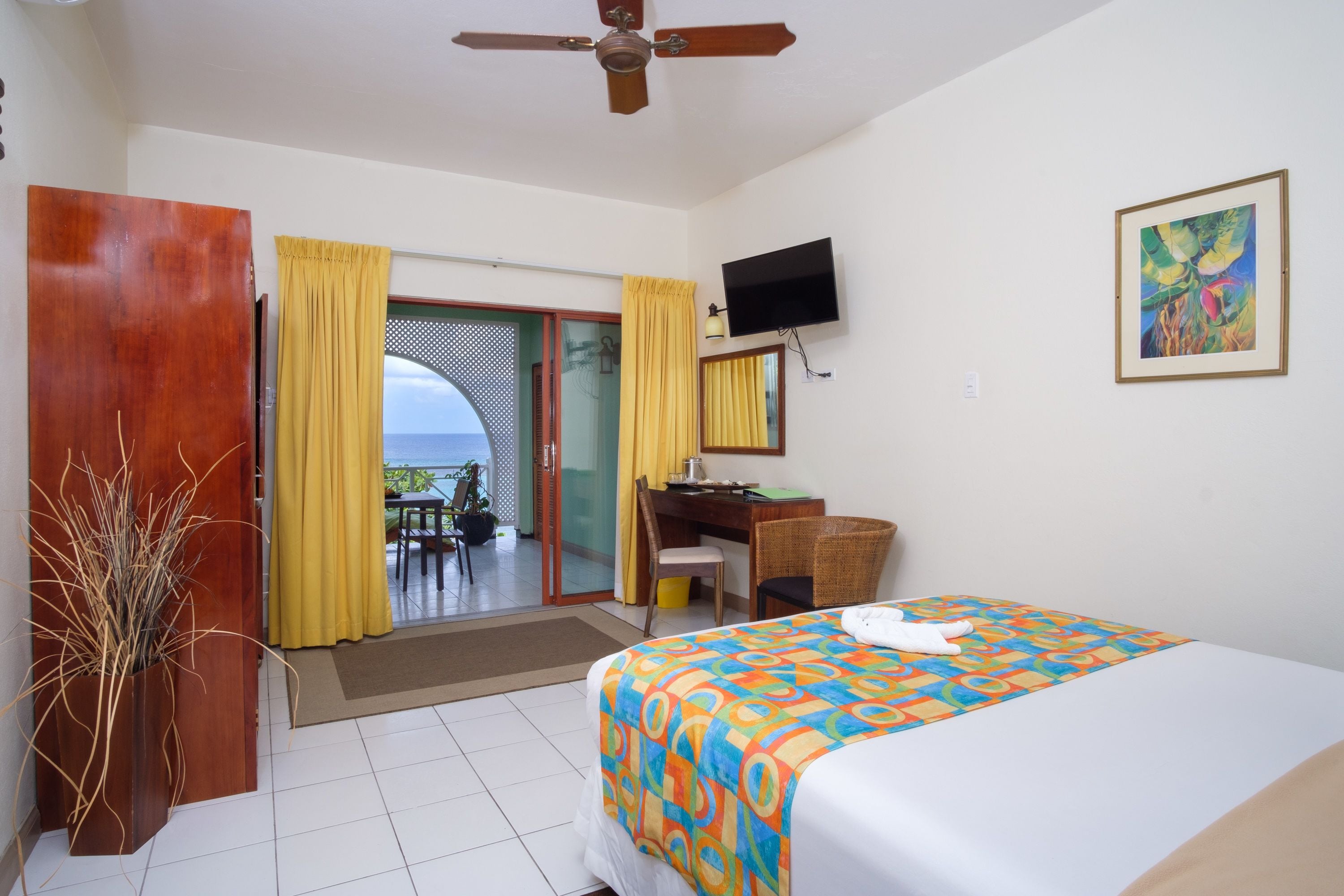 A hotel room with a bed, a desk, a chair, a TV, and a view of the sea.