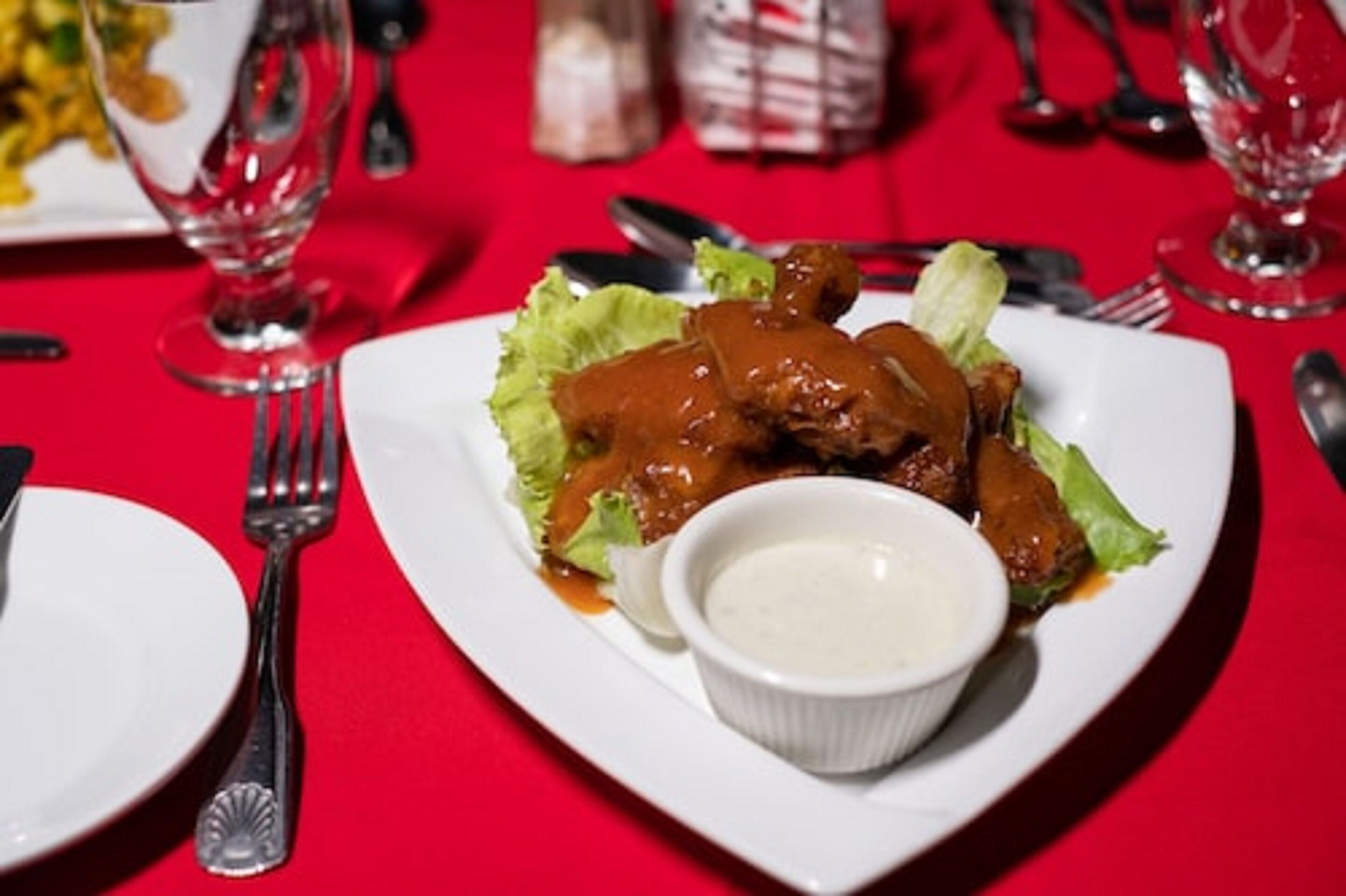 A plate of food with a sauce and a small bowl of sauce on a red tablecloth.