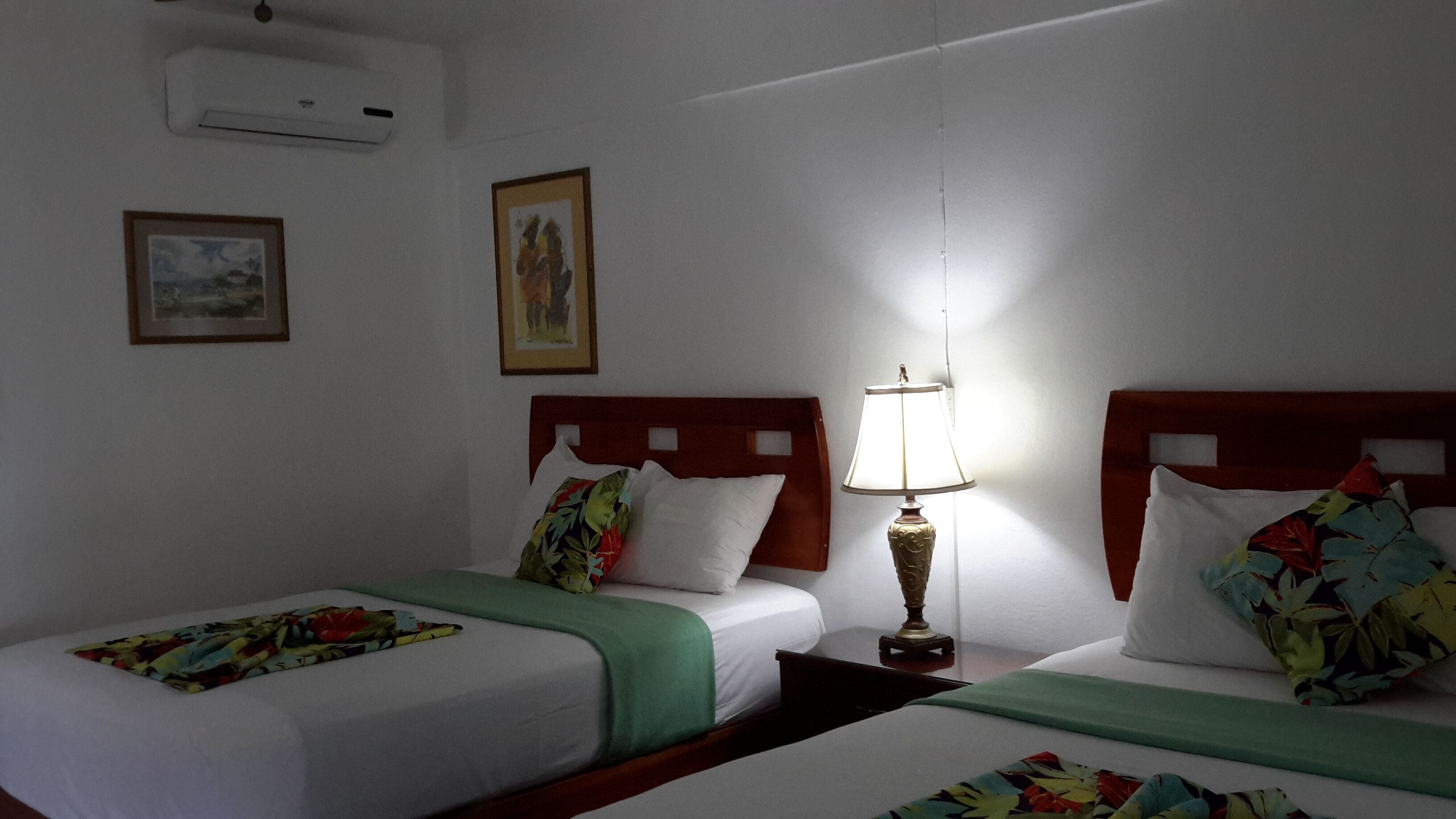 Une chambre d’hôtel avec deux lits, une table de chevet avec une lampe et deux tableaux encadrés au mur.