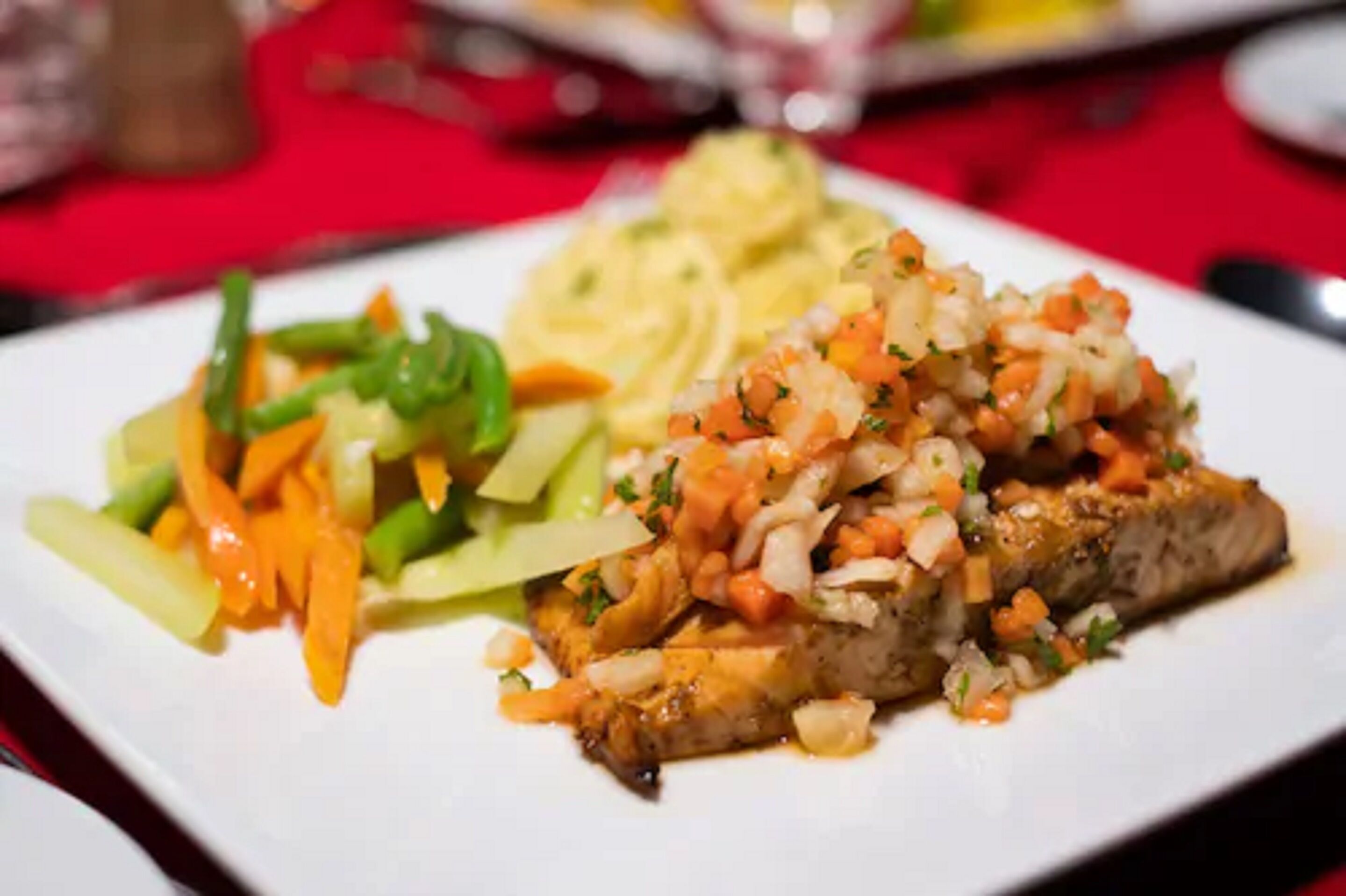 Een bord eten met een stuk vlees, belegd met blokjes groenten en een portie pasta.