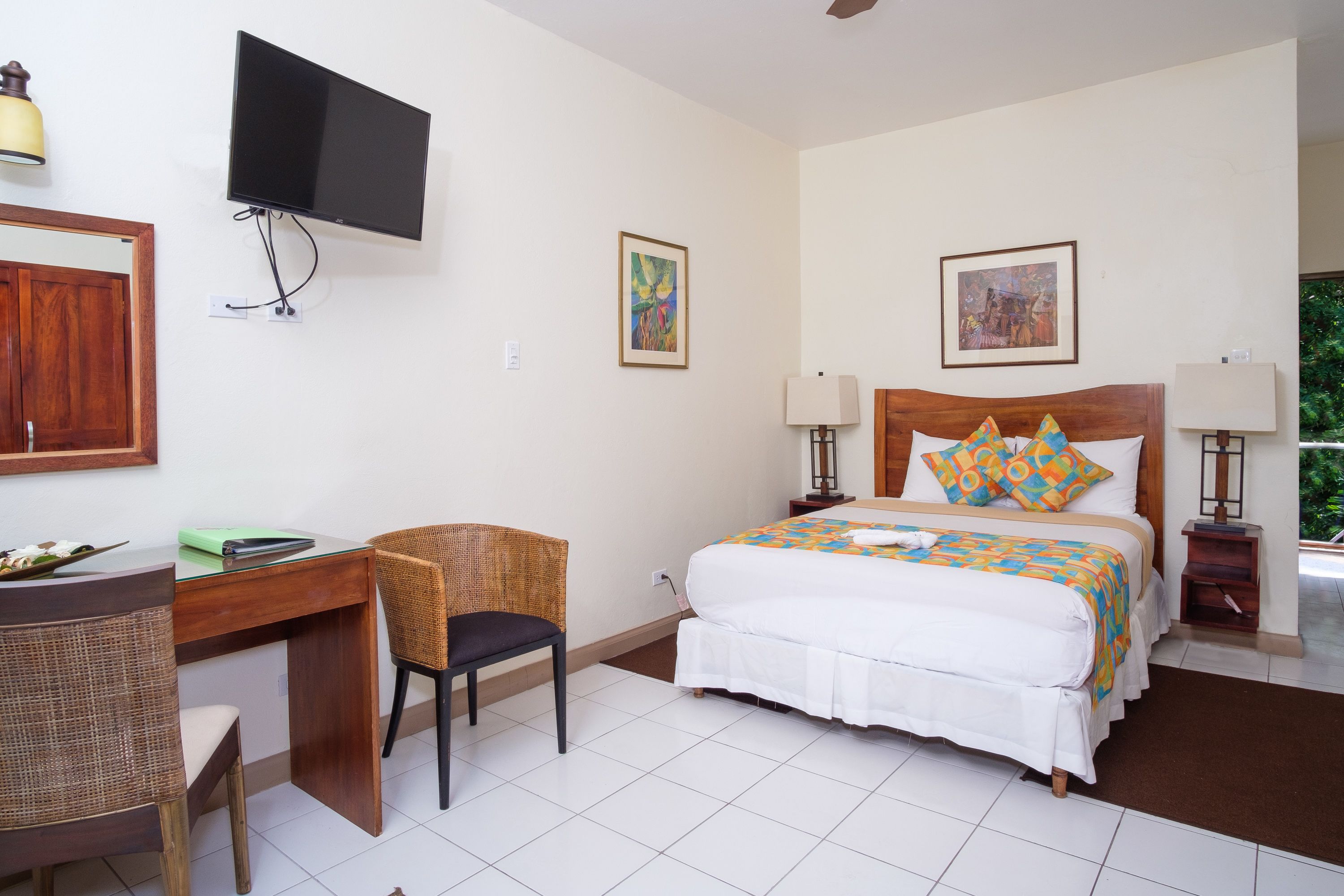 Habitació d'hotel amb llit, escriptori, cadira, televisió i obres d'art a les parets.