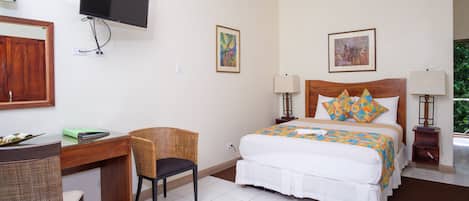 Habitación de hotel con cama, escritorio, silla, televisor y obras de arte en las paredes.