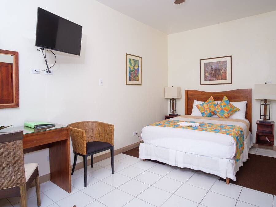Habitació d'hotel amb llit, escriptori, cadira, televisió i obres d'art a les parets.