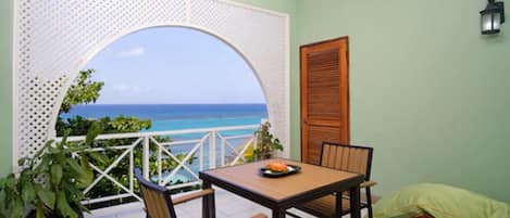 A balcony with a view of the ocean, a table with chairs, and a bed.