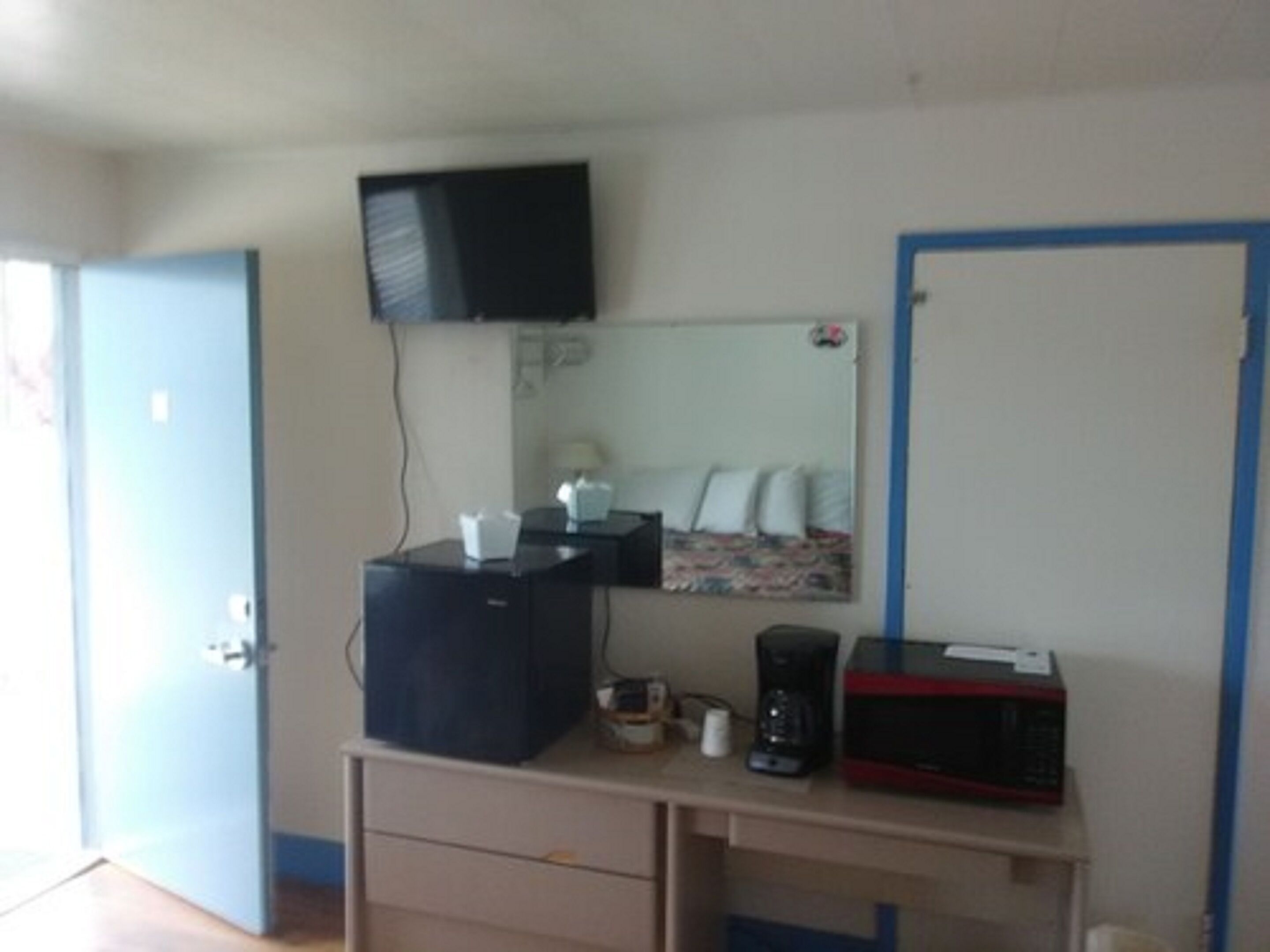 A small room with a desk, a television mounted on the wall, a mirror, and a door.