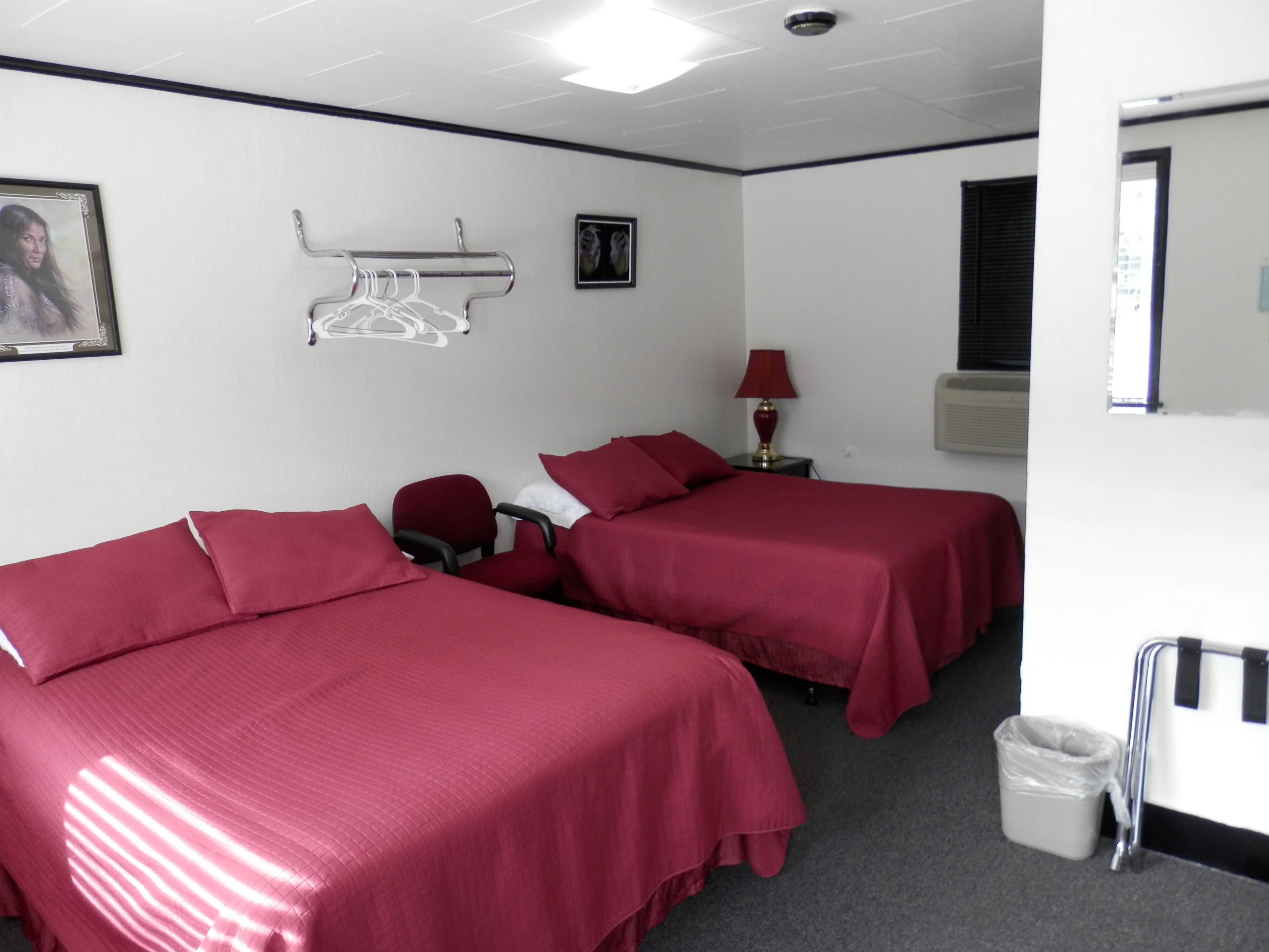 Quarto de hotel com duas camas, uma cadeira, um abajur e uma lixeira.