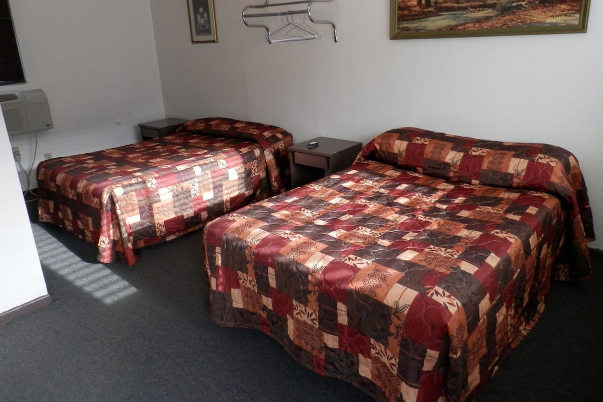 Quarto de hotel com duas camas, uma escrivaninha, uma cadeira, uma televisão e um quadro na parede.