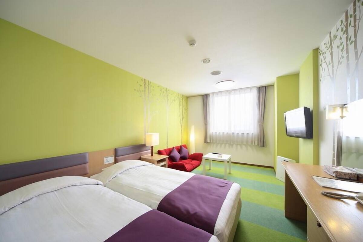 A hotel room with two beds, a desk, a chair, a television, and a window with curtains.