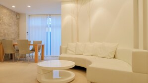 A modern living room with a white sofa, a round coffee table, and a dining area with chairs and a table. - Hotel Naturwald Furano (Furano)
